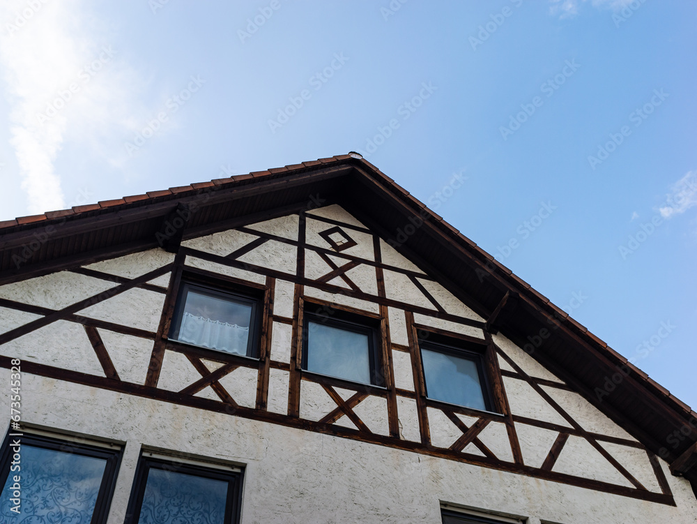 Facade of an old half timbered building. The traditional construction method used wooden beams and plaster material. Exterior wall with windows and the roof from a low angle.