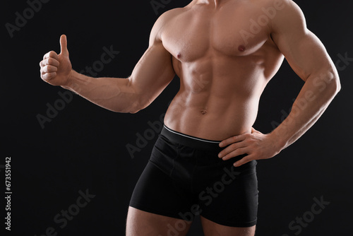 Young man in stylish underwear showing thumb up on black background, closeup