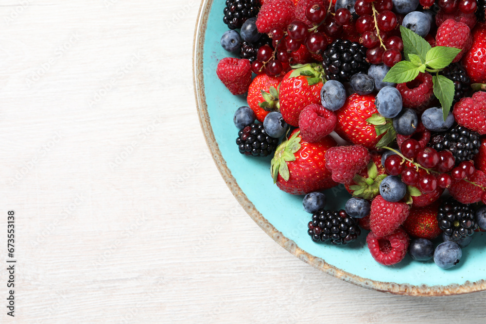 Many different fresh ripe berries in bowl on white wooden table, top view. Space for text Many different fresh ripe berries in bowl on white wooden table, top view. Space for text