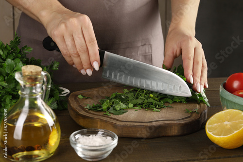 Woman cutting fresh parsley at wooden table, closeup