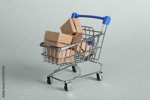 Small metal shopping cart with cardboard boxes on light background