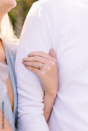 A close-up of a woman's arm as she clutches her fiance's arm. He wears a white shirt.