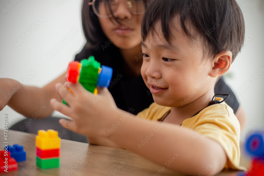 Asian cute brother and sister play with a toy block designer on the table in the living room at home. Concept of siblings bonding, friendship, and learning through play activity for kid development. Asian cute brother and sister play with a toy block designer on the table in the living room at home. Concept of siblings bonding, friendship, and learning through play activity for kid development.