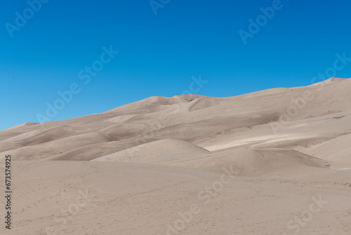 Arid sand dune landscape in direct sunlight with a bright blue sky at Great Sand Dune National Park in southern Colorado.