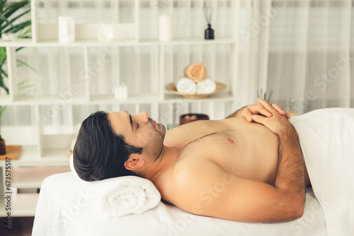 Caucasian man customer enjoying relaxing anti-stress spa massage and pampering with beauty skin recreation leisure in day light ambient salon spa at luxury resort or hotel. Quiescent