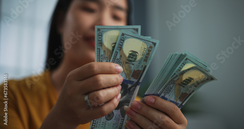 Portrait of young Asian woman enjoy counting cash dollars banknotes on sofa in the living room at home.