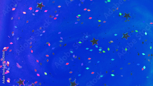 Abstract background. Shimmering liquid paint. Iridescent glitter particles. Decorative star rhombus shape sequins floating on neon blue ink surface.