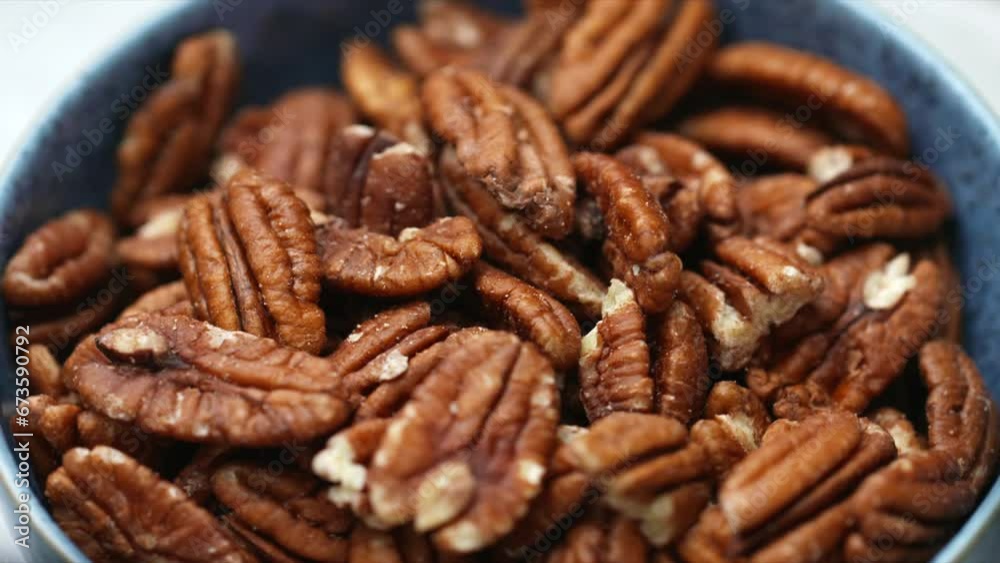 Pecan nuts rotating in blue bowl. whole food raw pecans. HD shallow depth of field image of wholegrain foods for plant-based and vegan diet and recipes.