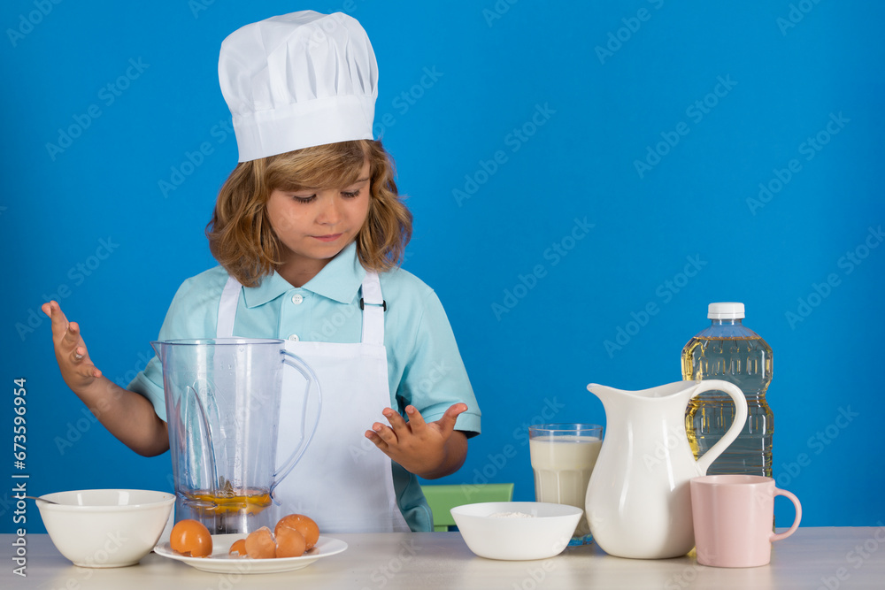 Portrait of a 7, 8 years old child in cook cap and apron making fruit salad and cooking food in kitchen. Cute little blonde happy smiling chef. Portrait of a 7, 8 years old child in cook cap and apron making fruit salad and cooking food in kitchen. Cute little blonde happy smiling chef.
