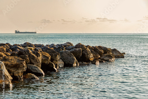 Seascape. A breakwater made of stones. A beach with a breakwater made of large stone boulders. View of the sea breakwater made of stones. A dam near the seashore in summer.