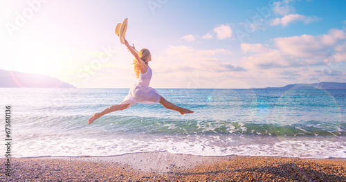 Happy tourist woman in a white dress enjoys beautiful beach at sunset