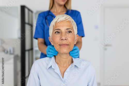 Friendly woman doctor wearing gloves checking sore throat or thyroid glands  touching neck of senior female patient visiting clinic office. Thyroid cancer prevention concept