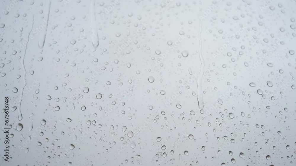 A slow-motion close-up view of heavy raindrops is seen through a window glass. A slow-motion close-up view of heavy raindrops is seen through a window glass.