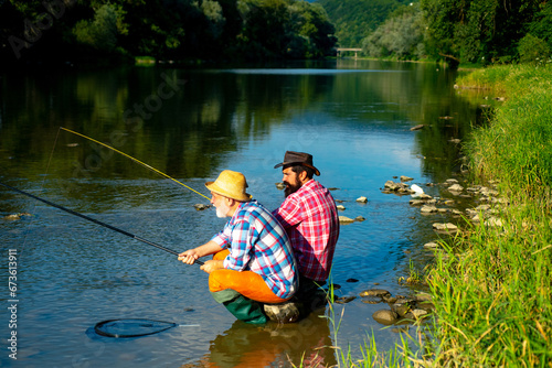 Two men friends anglers fishing. Flyfishing angler makes cast, standing in river water. Old and young fisherman.