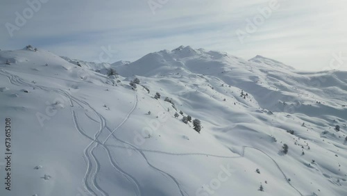 Aerial epic snow covered glacier mountain range scenery, fllying over alpine summits with ski tracks on sunny day