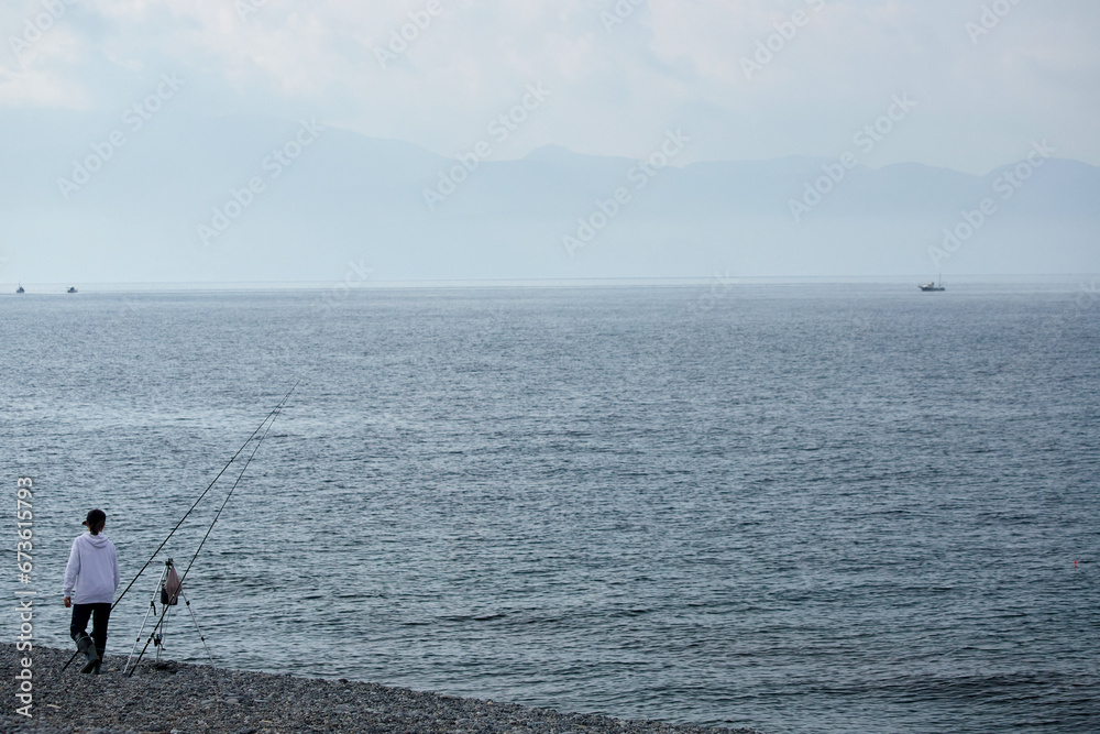 朝の海岸で海釣している若い女性の姿