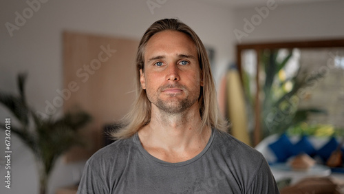 Happy male person face home portrait. Blue eyes looking at camera close up. Joyful bristle surfer man long hair. Smiling shy guy. Kind casual people. Young adult hippie inside house. Hipster hairstyle