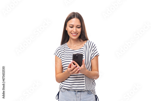 young positive brunette lady with straight hair in glasses dressed in a striped t-shirt is watching video on the phone on a white background with copy space