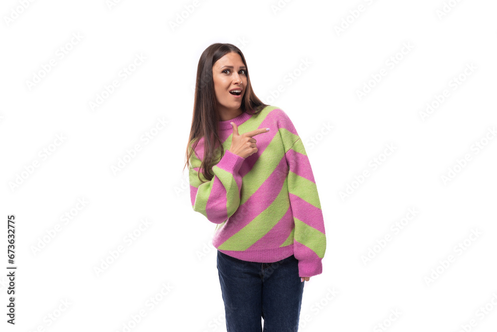 stylish cheerful young brunette woman in a striped pink sweater points her finger to the side on a white background with copy space stylish cheerful young brunette woman in a striped pink sweater points her finger to the side on a white background with copy space