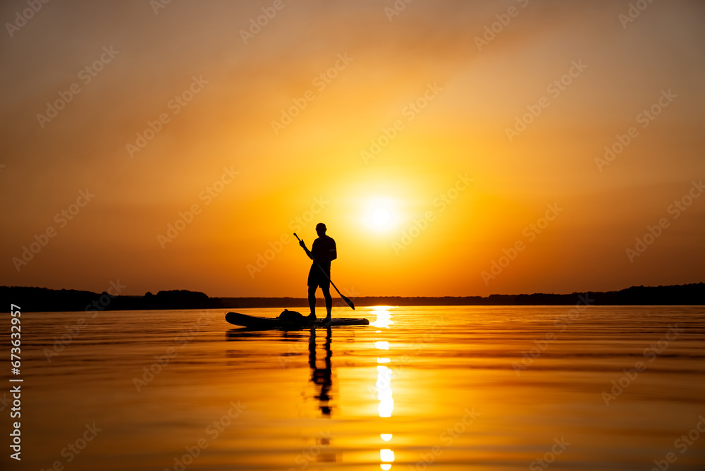 A person standing on a paddle board in the water. A Serene Moment: Stand-Up Paddleboarding on the Calm Waters
