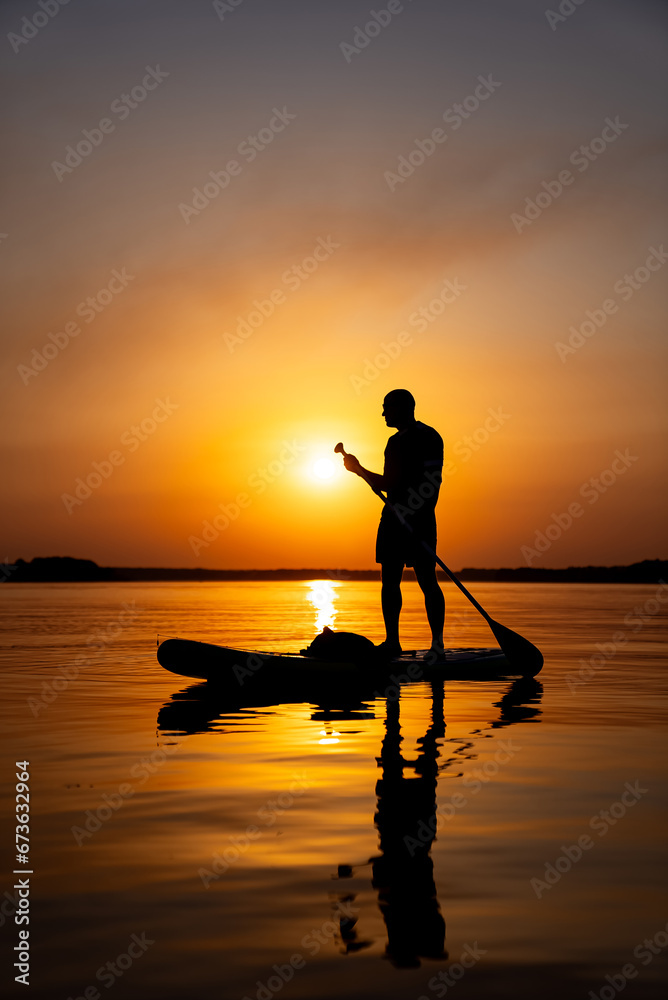 A Serene Moment: Man Standing on Paddle Board in Crystal Clear WatersA man standing on a paddle board in the water.