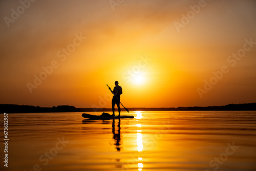 A person standing on a paddle board in the water. A Serene Moment: Stand-Up Paddleboarding on the Calm Waters © Vadim