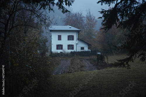 An isolated house in the forest near Lake Cei, at blue hour, in the Northern Italy, during a rainy autumnal day
