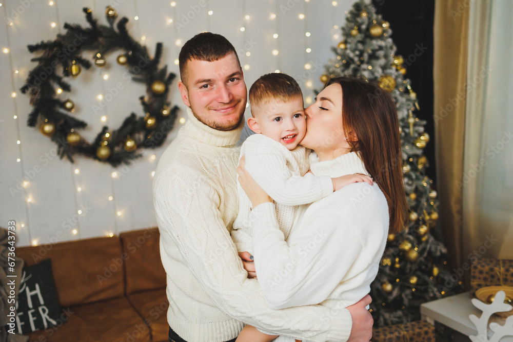 A happy young family with a small child is celebrating the New Year at home near the Christmas tree. Christmas with the family, New Year - time to celebrate. A happy young family with a small child is celebrating the New Year at home near the Christmas tree. Christmas with the family, New Year - time to celebrate.