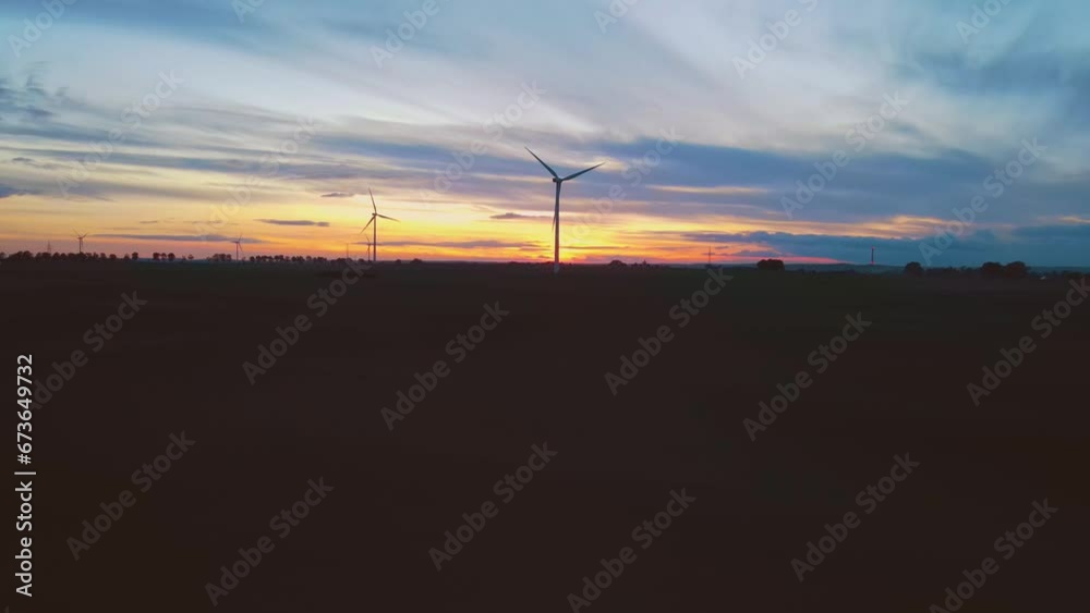 Large wind turbines with blades in field aerial view windmills silhouette at amazing cloudy colorful sunset. Electricity, ecological saving and alternative power source Large wind turbines with blades in field aerial view windmills silhouette at amazing cloudy colorful sunset. Electricity, ecological saving and alternative power source
