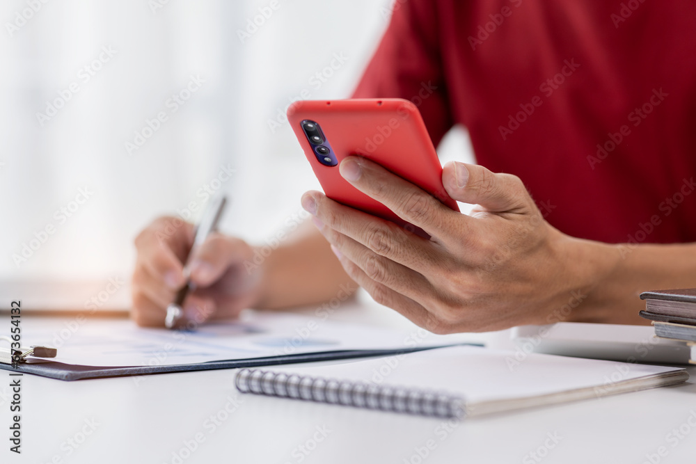 Fototapeta premium Close up hand of man writing notes while making phone call and using laptop at home