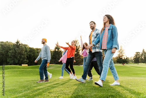 Different multiracial friends wearing stylish colorful clothes walking together in park, talking