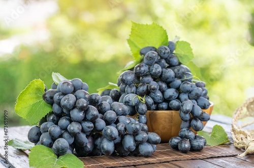 Black grapes with leaves in wooden basket on wooden table in garden, Black or Purple grape with leaves in blur background.