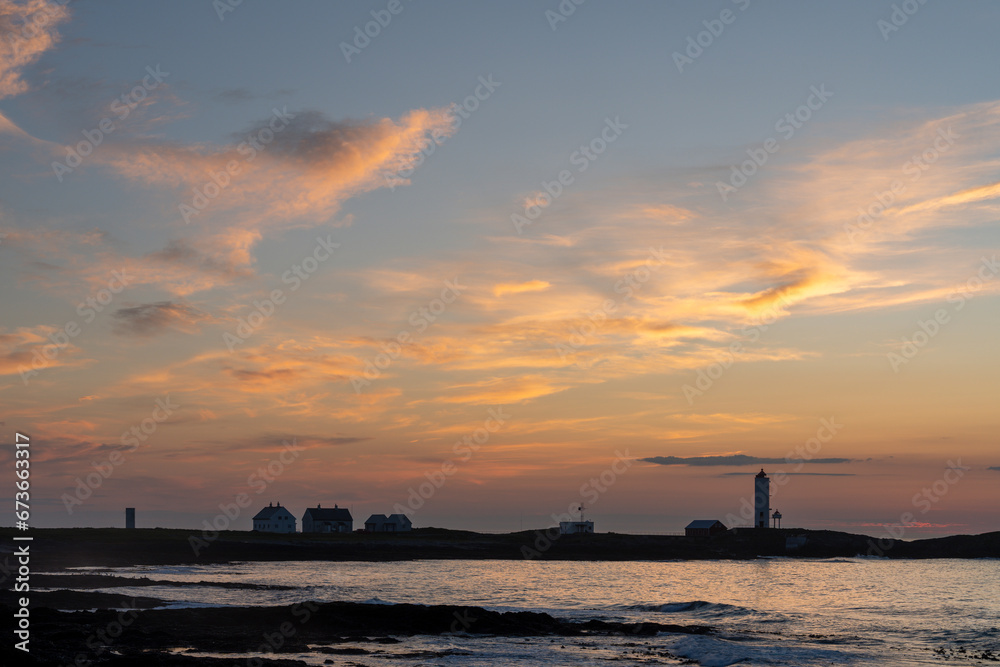 Kjolnes lighthouse on the rocky shores of Barents Sea in soft and colorful evening light after sunset