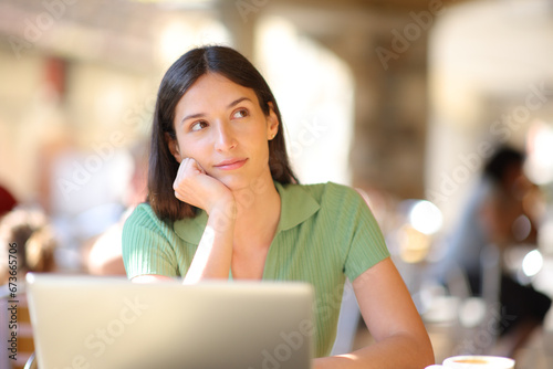 Woman with laptop thinking looking at side in a bar © Antonioguillem