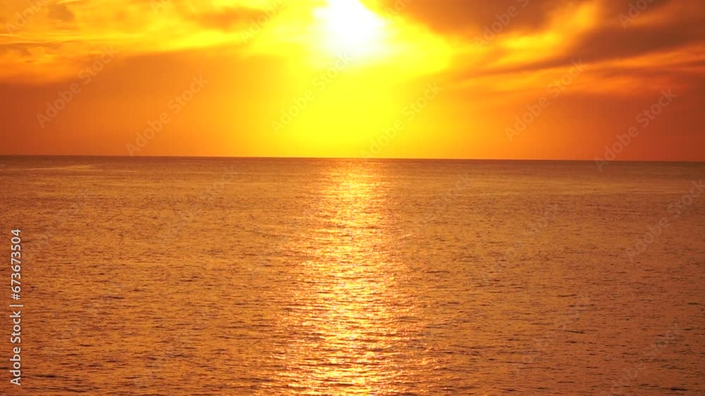 A red burning sunset over sea with rocky volcanic cliff. Abstract nature summer ocean sea background. Small waves on golden warm water surface with bokeh lights from sun. Weather and climate change A red burning sunset over sea with rocky volcanic cliff. Abstract nature summer ocean sea background. Small waves on golden warm water surface with bokeh lights from sun. Weather and climate change
