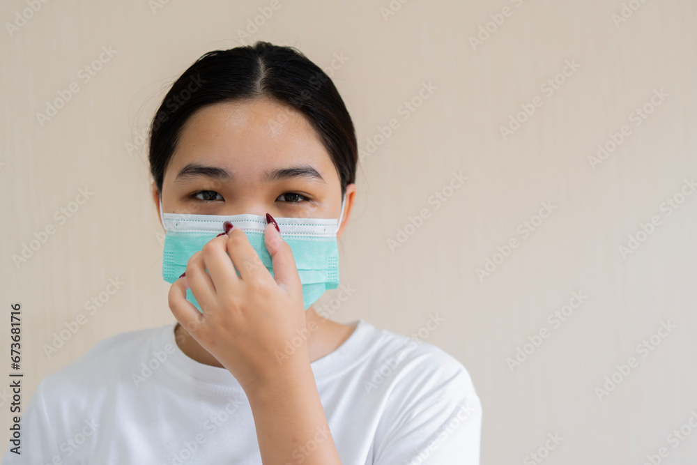 Portrait of a young girl in a medical mask and adjusting her mask isolated on a light beige wall background.