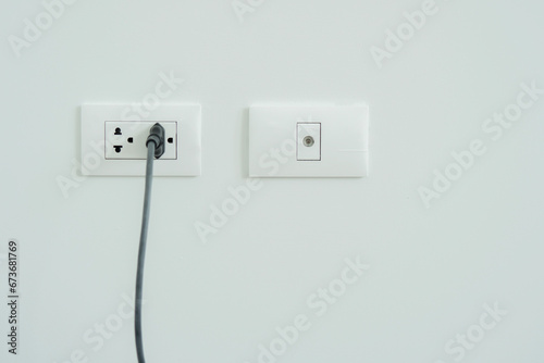 White electrical plug in the electric double socket and cabel socket on white wall.