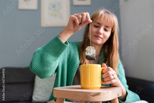 Smiling woman dipping teabag in mug at home