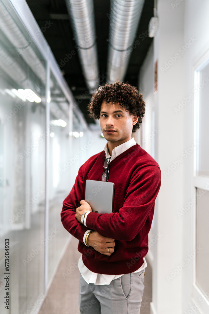 Young businessman with laptop standing in corridor at office Young businessman with laptop standing in corridor at office