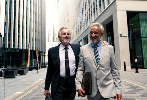 Happy senior businessmen walking and talking with each other amidst financial buildings photo