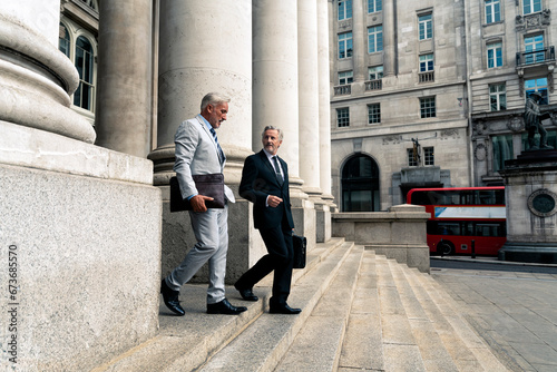 Businessmen moving down on steps near architectural columns photo