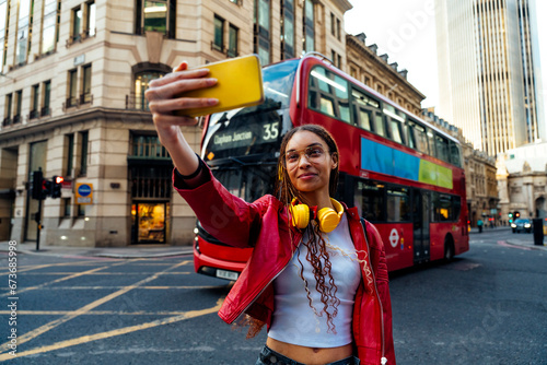 Woman with headphones taking selfie through smart phone on road in city