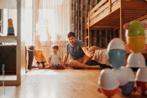 Cheerful father playing bowling game with sons at home photo