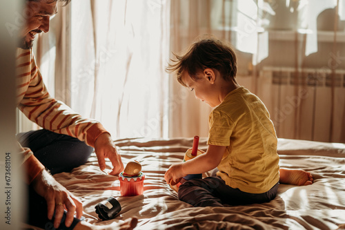 Cute boy playing with father on bed at home photo