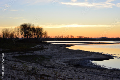 amazing sunset on the lake with bare trees on the coast 