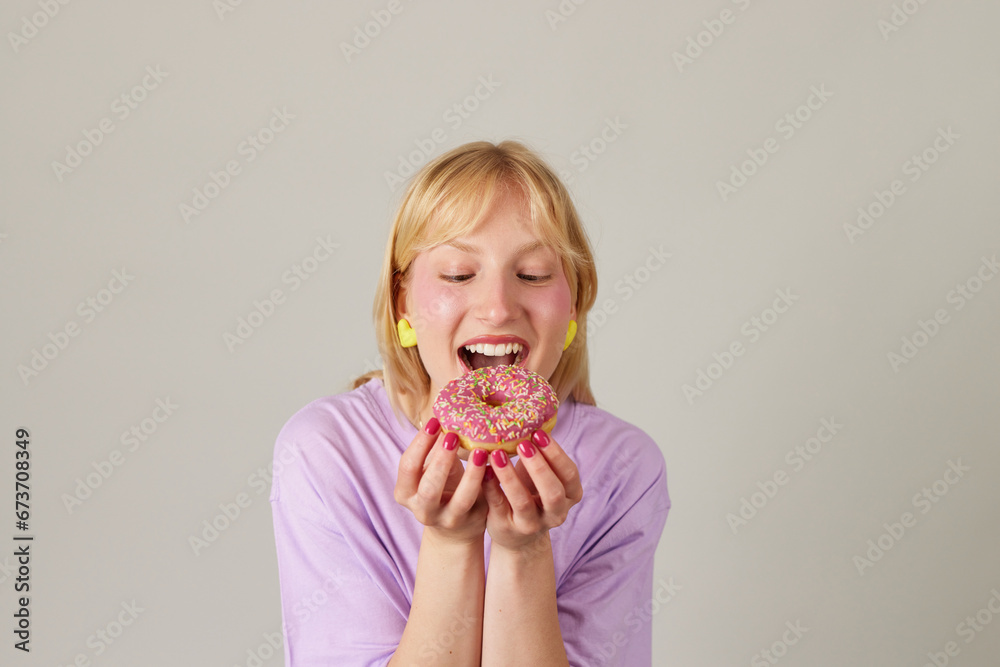Young woman holding and enjoys eating donut with pink icing
