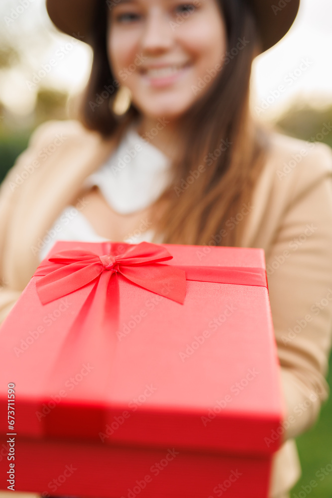 Portrait of charming lady in beige classic coat holding present box in autumn park at sunset. Vertical frame. Portrait of charming lady in beige classic coat holding present box in autumn park at sunset. Vertical frame.