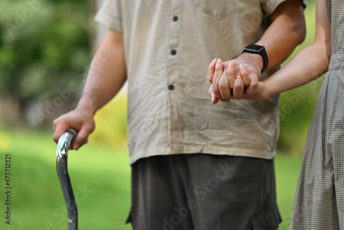 Affectionate adult daughter holding hand of mature father while walking at the green park