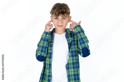 Caucasian teen boy wearing plaid shirt covering ears with fingers with annoyed expression for the noise of loud music. Deaf concept.