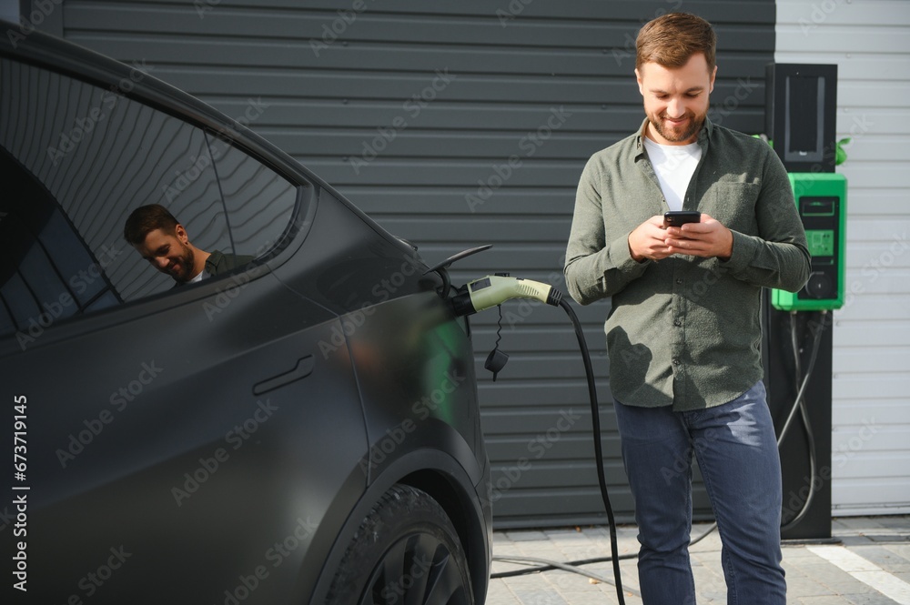 A man stands near a charging station and charges his electric car